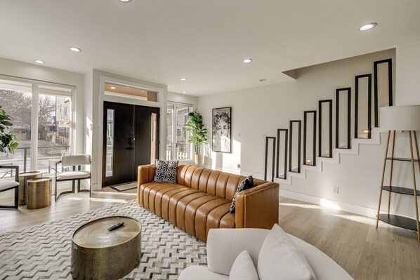 A modern living room with a leather sofa, a coffee table, and a staircase with framed mirrors.