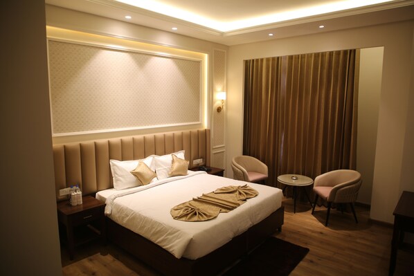 A hotel room with a large bed, a bedside table with a lamp, two chairs, a small round table, and a window with curtains. - Country Yard Hotel (Nakodar)