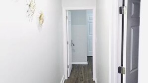 Un pasillo estrecho con paredes blancas y suelo de madera, que conduce a una habitación con una puerta.