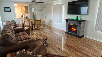 Una sala de estar con chimenea, un televisor montado en la pared y un comedor con sillas y una mesa.