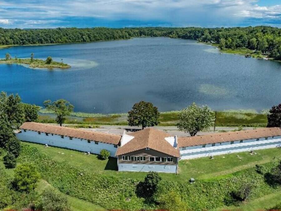 Un edificio grande y rectangular con techo central, rodeado de exuberante vegetación y un lago.