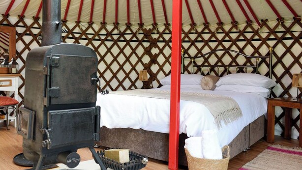 Una carpa con una cama, una silla de madera, una mesita y una estufa.