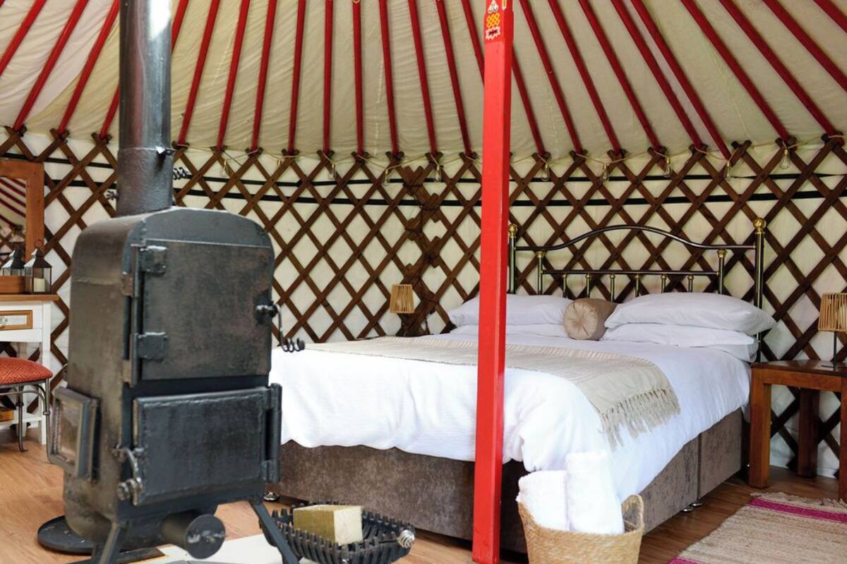 A tent with a bed, a wooden chair, a small table, and a stove.