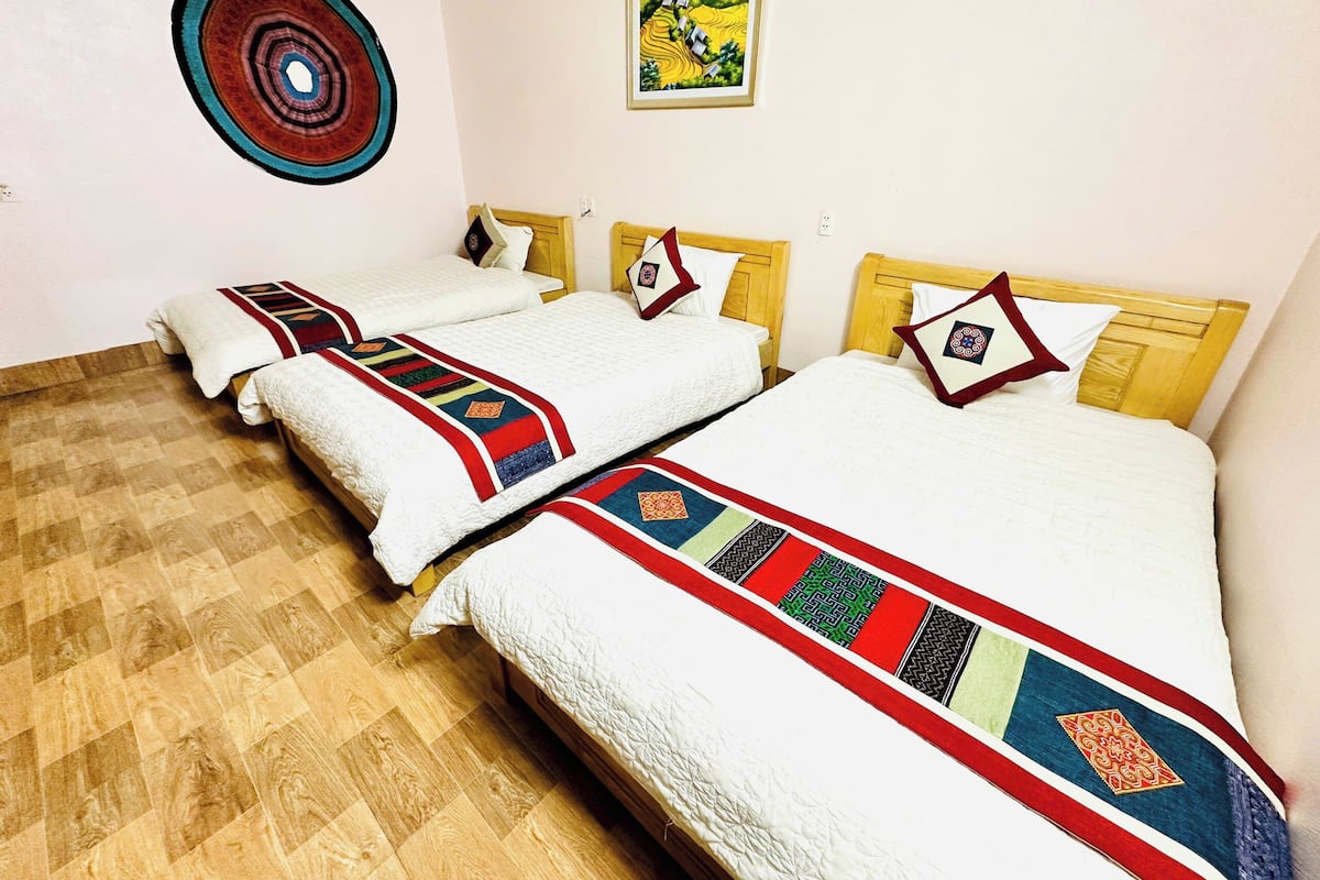 A hotel room with three beds, each with a white quilt and a colorful blanket.