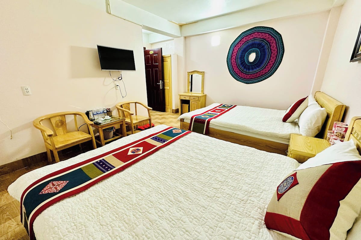 A hotel room with two beds, a desk, a chair, a television, and a decorative wall hanging.