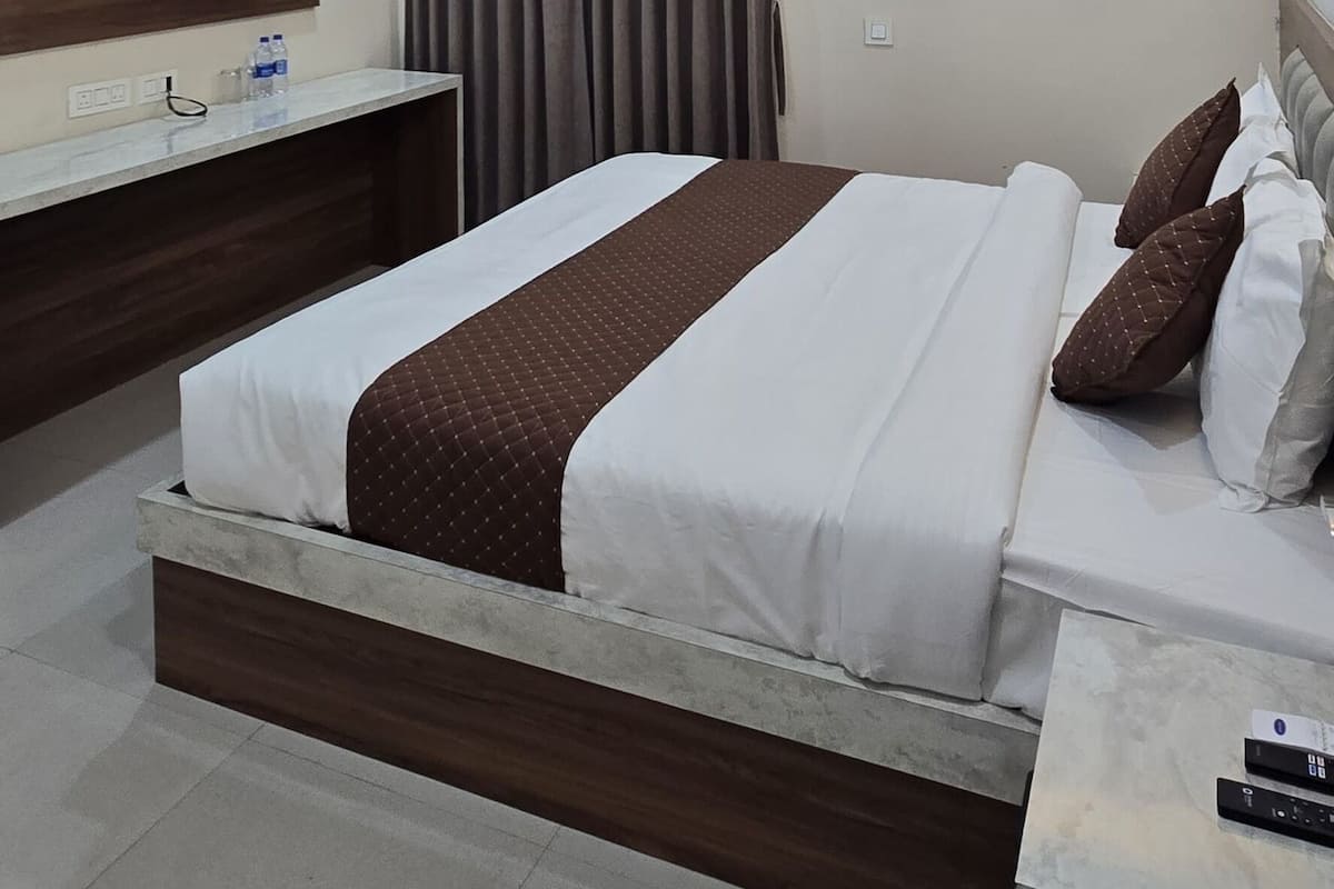 A modern hotel room with a large bed, a ceiling fan, an air conditioning unit, a flat-screen TV, and a bedside table with a remote control.