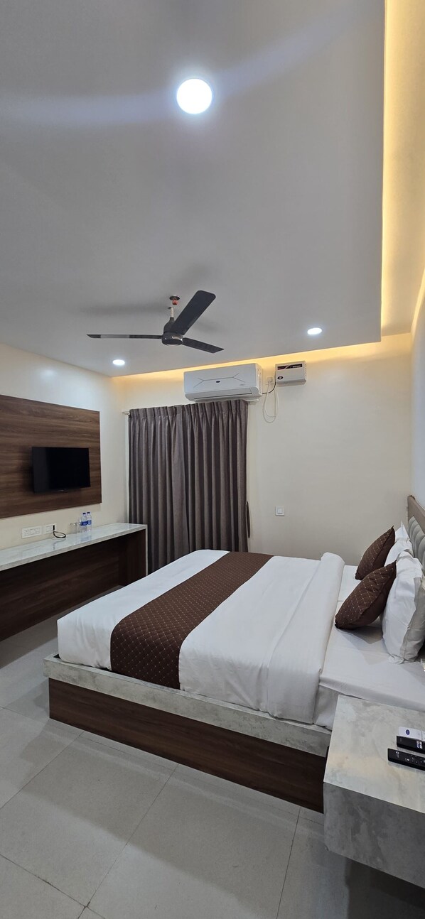 A modern hotel room with a large bed, a ceiling fan, an air conditioning unit, a flat-screen TV, and a bedside table with a remote control. - Hotel Ultimate One (Bhubaneshwar)
