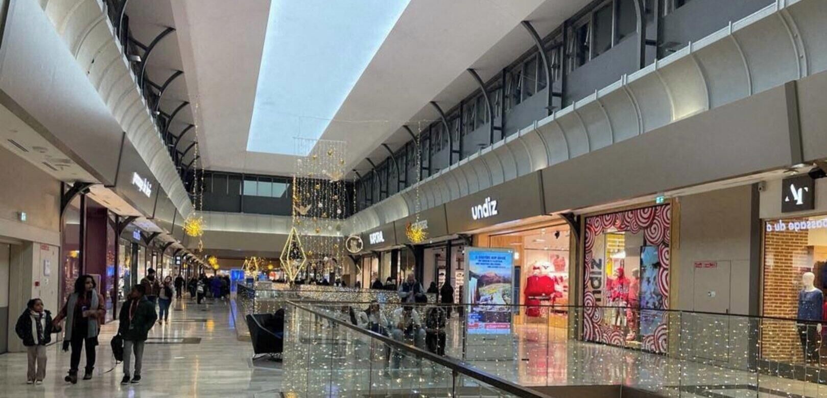 L’intérieur d’un centre commercial, avec une rambarde en verre, des boutiques et des décorations festives.