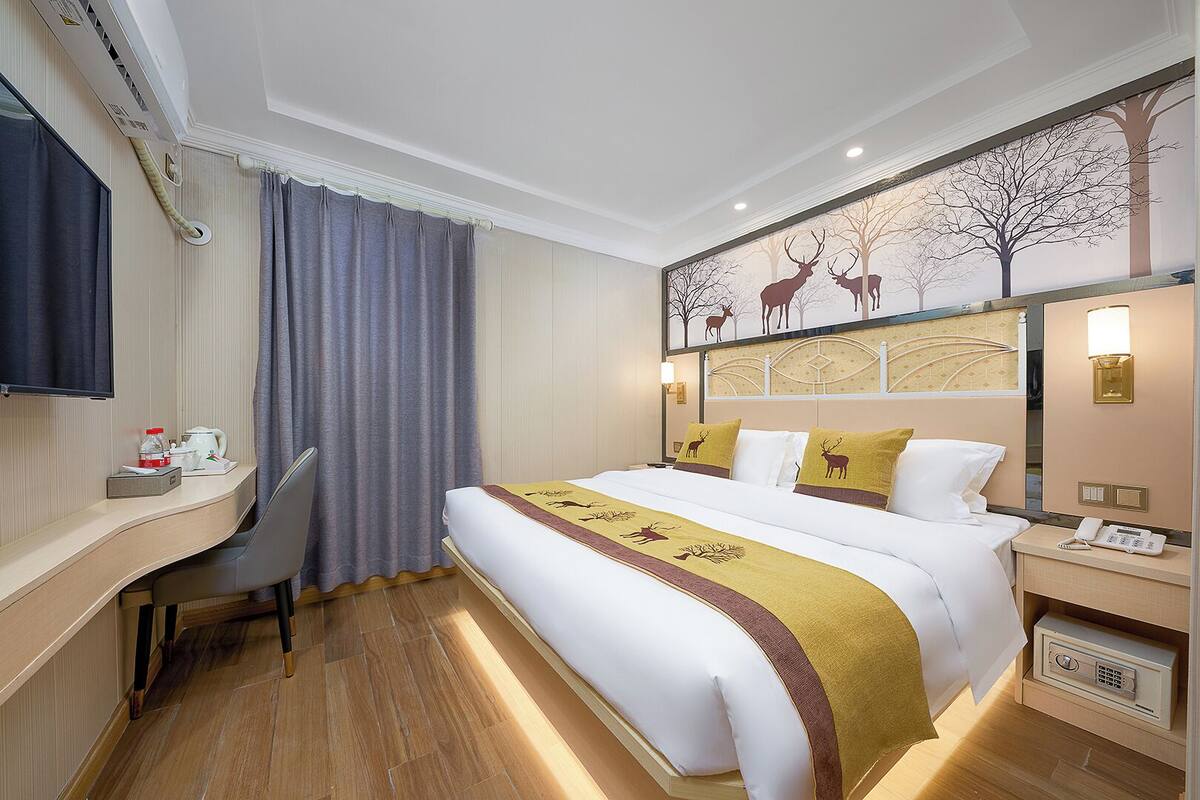 Une chambre d’hôtel avec un lit, un bureau, une chaise et un tableau représentant des cerfs accroché au mur.