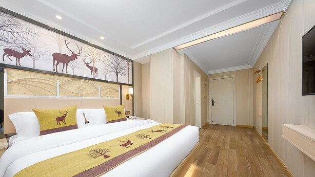 A hotel room with a large bed, a wall mural of deer, and a hallway leading to another room. - Yushe Hotel  (Guangzhou)