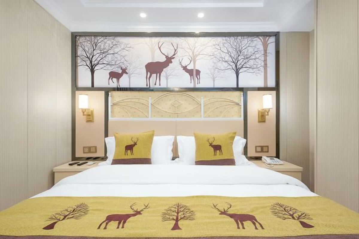 A hotel room with a bed featuring a deer and tree design, a headboard with integrated lighting, and bedside tables with lamps.