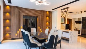 Un comedor moderno con una mesa rectangular rodeada de sillas, una cocina con encimera de mármol e iluminación empotrada en el techo.