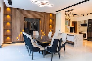 A modern dining area with a rectangular table surrounded by chairs, a kitchen with a marble countertop, and a ceiling with recessed lighting.