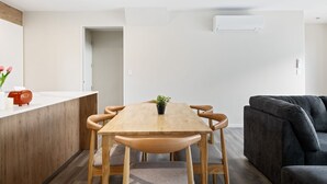 A modern living room with a wooden dining table, a sofa, and a kitchen area with a countertop and a toaster. - Full-sized 3 Bedroom Townhouse - Walking distance to Stadium (Christchurch)