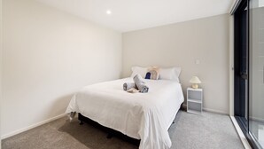 A bedroom with a bed, a nightstand, and a window. - Full-sized 3 Bedroom Townhouse - Walking distance to Stadium (Christchurch)