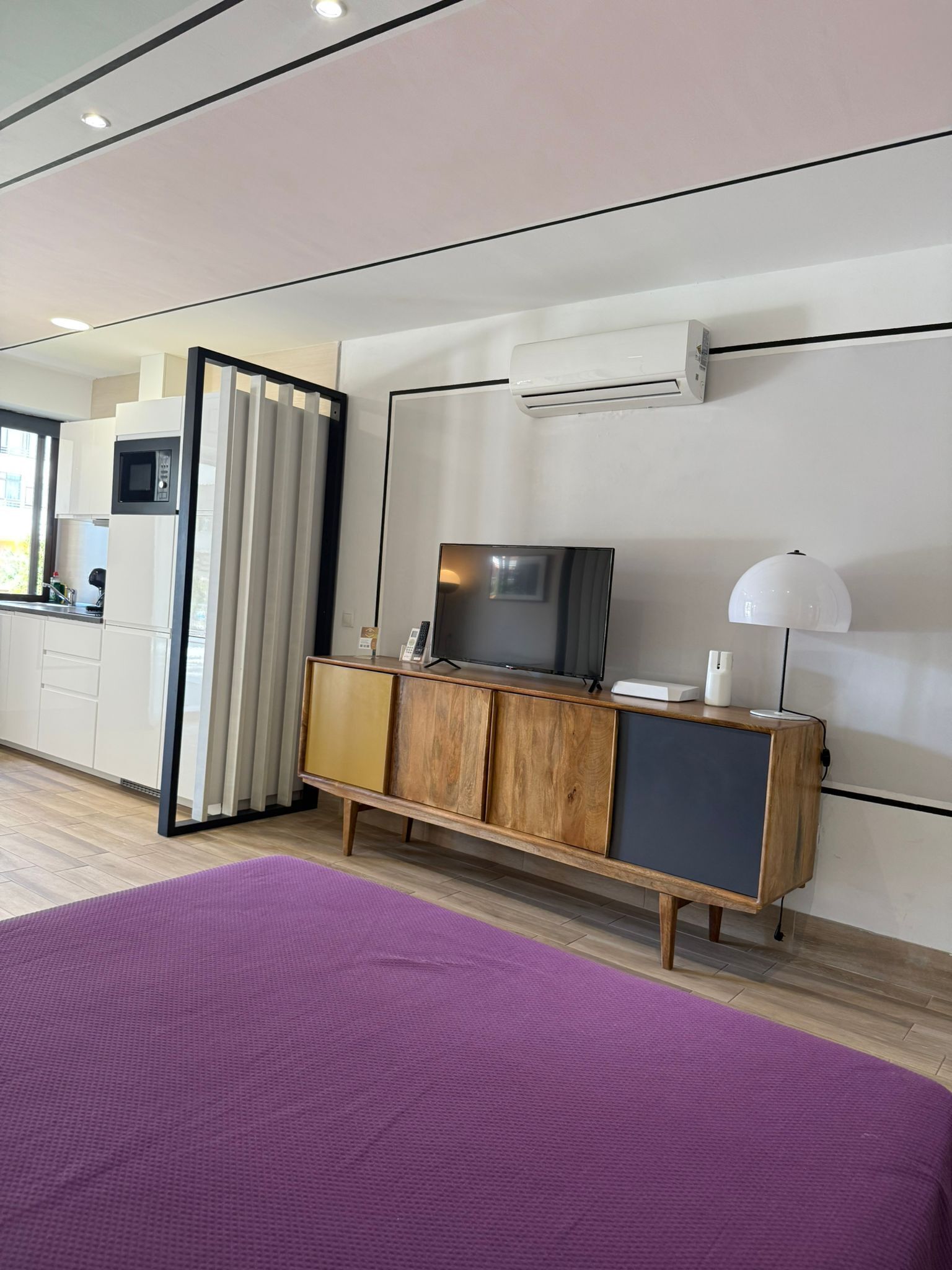 Une chambre d’hôtel moderne avec un grand lit, une armoire en bois avec un téléviseur, un petit coin cuisine et une fenêtre avec des rideaux.