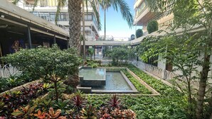 Un cortile con una fontana al centro, circondato da vegetazione rigogliosa e palme.