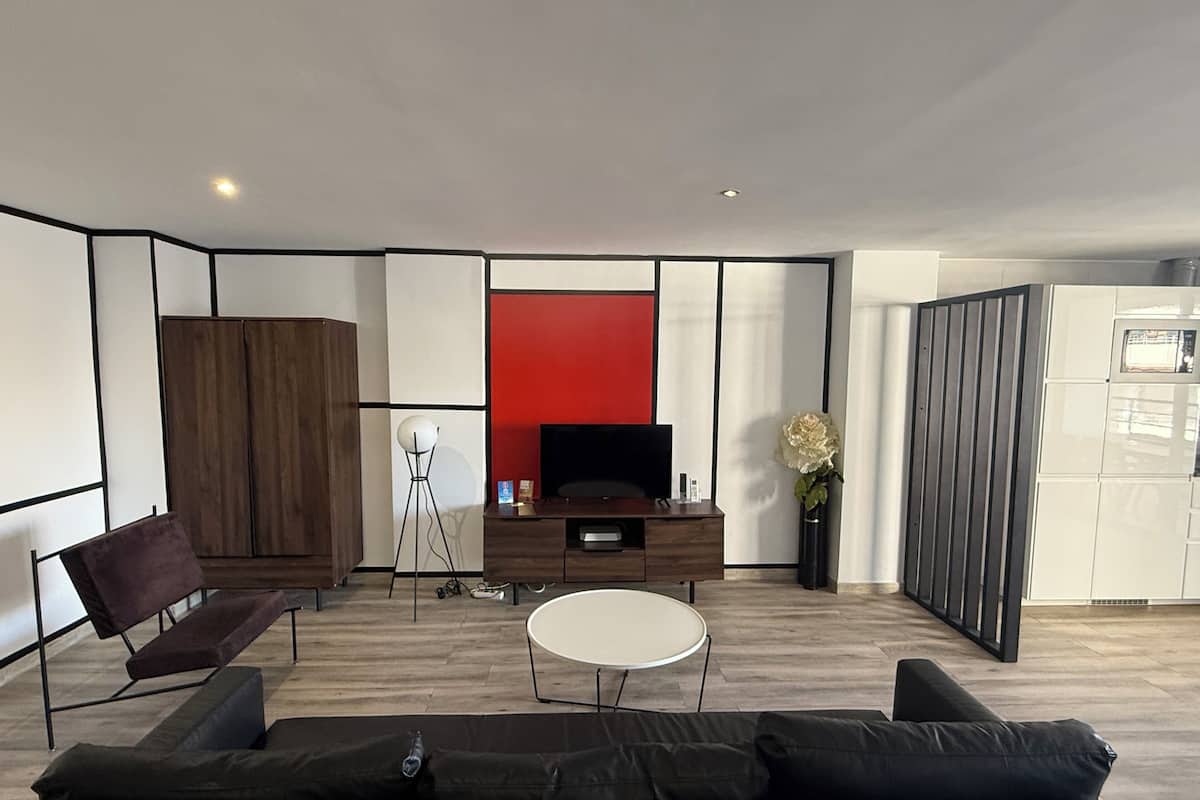 A modern living room with a sofa, a coffee table, a TV, and a red accent wall.