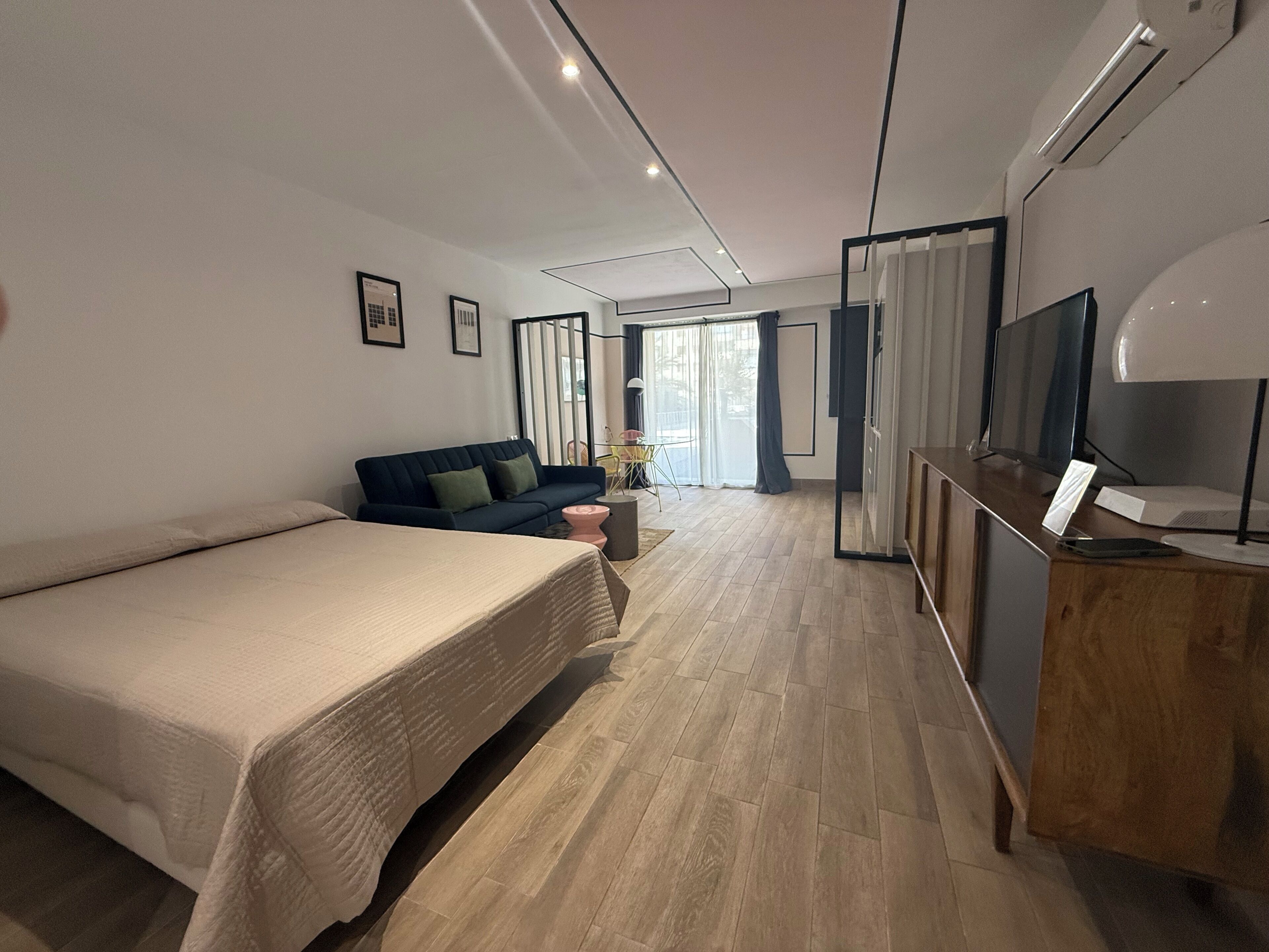 A modern hotel room with a large bed, a sofa, a desk with a computer, and a TV.