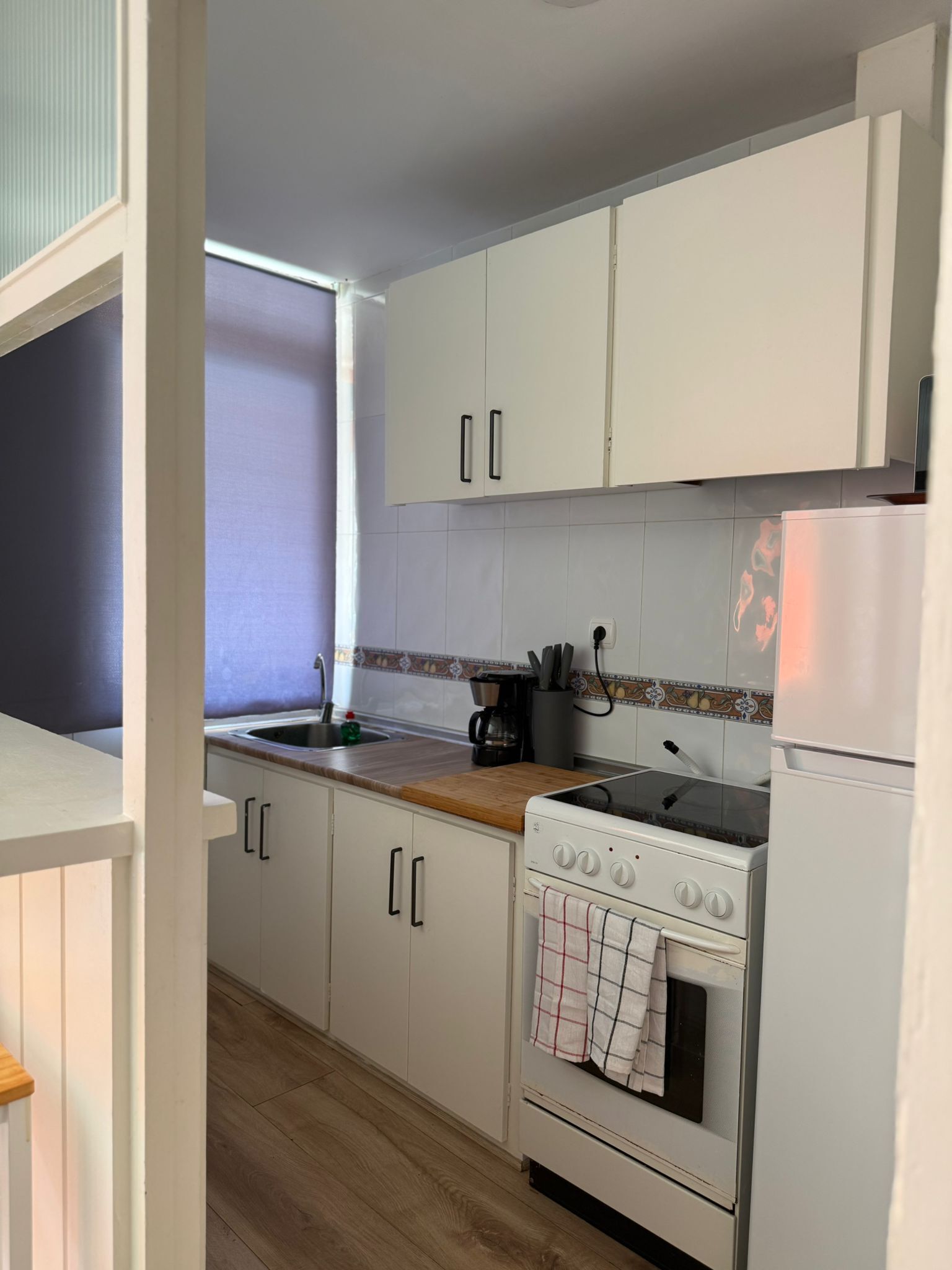 A compact kitchen with white cabinets, a wooden countertop, a stove, and a refrigerator.