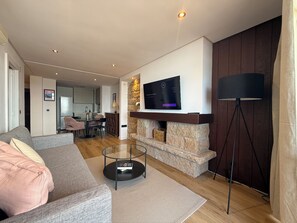 Una sala moderna con un sofá, una chimenea, un televisor y un comedor al fondo.