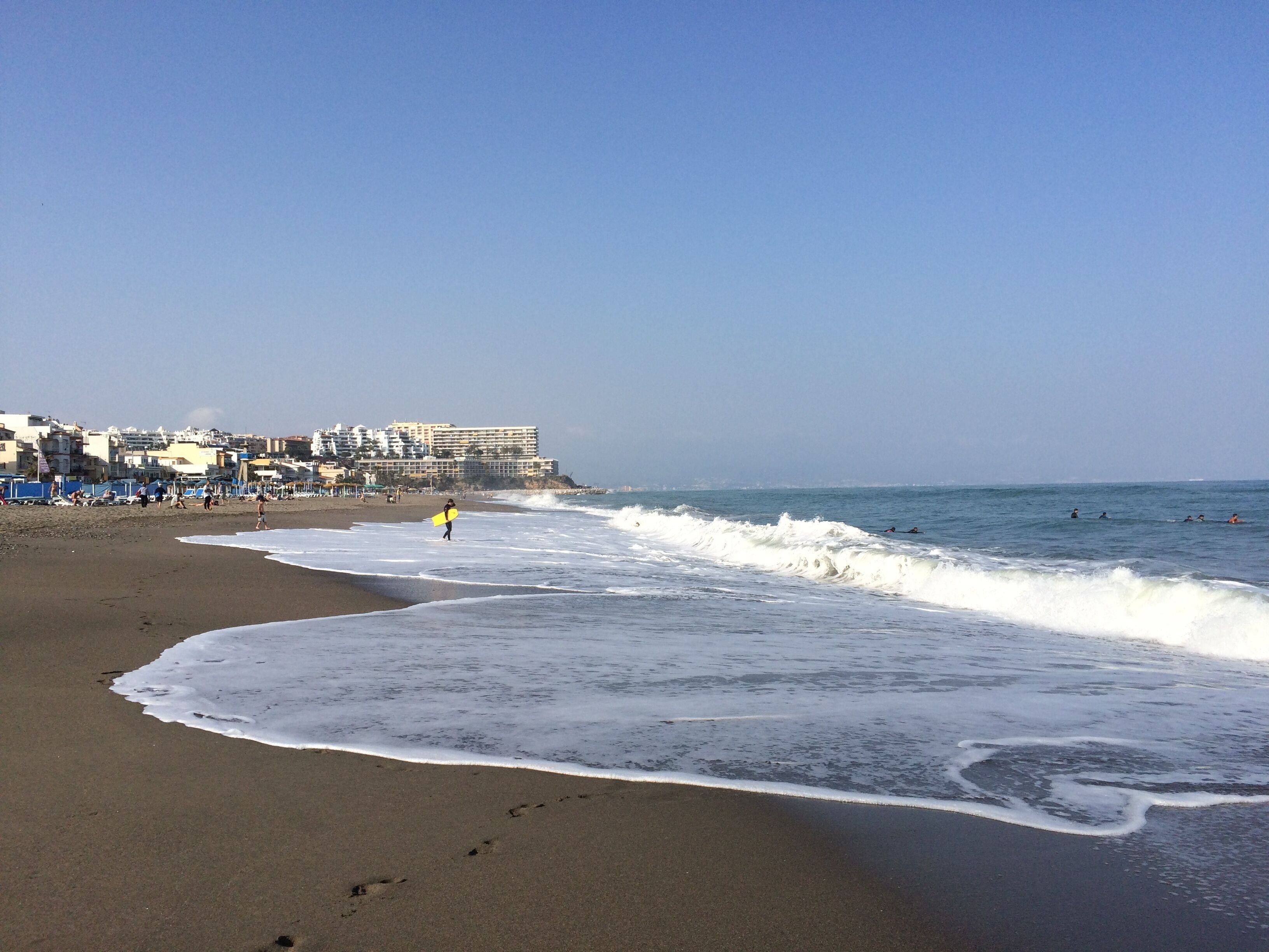 A beach with a sandy shore, waves, and a building in the background.