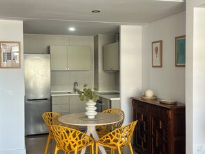 Une cuisine compacte dotée d’appareils électroménagers modernes, un coin repas avec des chaises jaunes et une petite table.