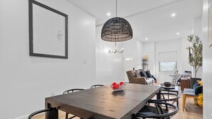 Un espace repas moderne avec une table en bois, des chaises noires et un luminaire suspendu noir en fibres tressées.