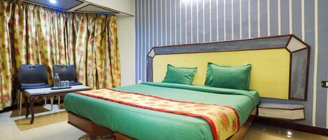 A hotel room with a large bed, a desk with chairs, and a curtain with a floral pattern.