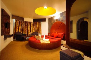 A circular red sofa with cushions, a small table, a chair, and a mirror. - Hotel Sapphire Paradise (Ooty)