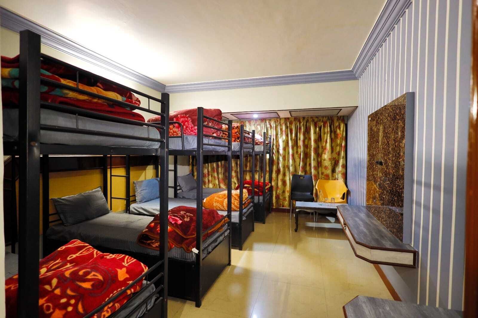 A dormitory room with bunk beds, a desk, a chair, and a curtain.