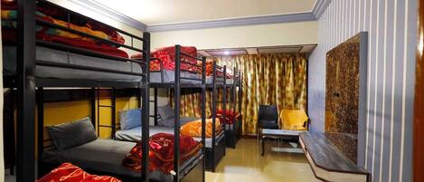 A dormitory room with bunk beds, a desk, a chair, and a curtain.