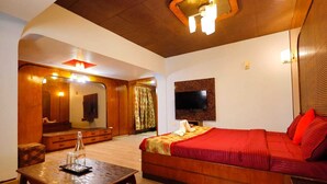 Ein Hotelzimmer mit Holzboden, einem großen Bett mit roter Bettwäsche, einem an der Wand befestigten Fernseher, einem Holztisch mit einem Glas und einem Spiegel in der Ecke.