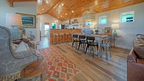 Ein geräumiger Wohnbereich mit Holzboden, einem Esstisch mit Stühlen und einer Küchenzeile mit Barhocker.