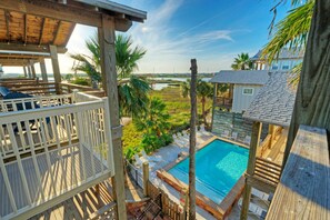 A wooden deck with a pool, lounge chairs, and a view of a water body and greenery. - Relaxed Port Aransas Home Near Beach, Dining, and Island Fun | At Last (Port Aransas)