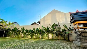 A courtyard with a patterned paving, a large building with a sloped roof, and a small structure with ornate details. - Sekar Tunjung Guest House Seminyak (Denpasar)