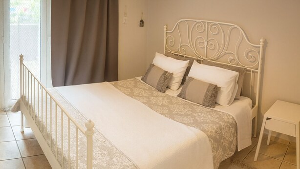 A bedroom with a bed, curtains, a bedside table, and wall decorations. - Georgias house 7 min from Athens airport (Spata-Artemida)