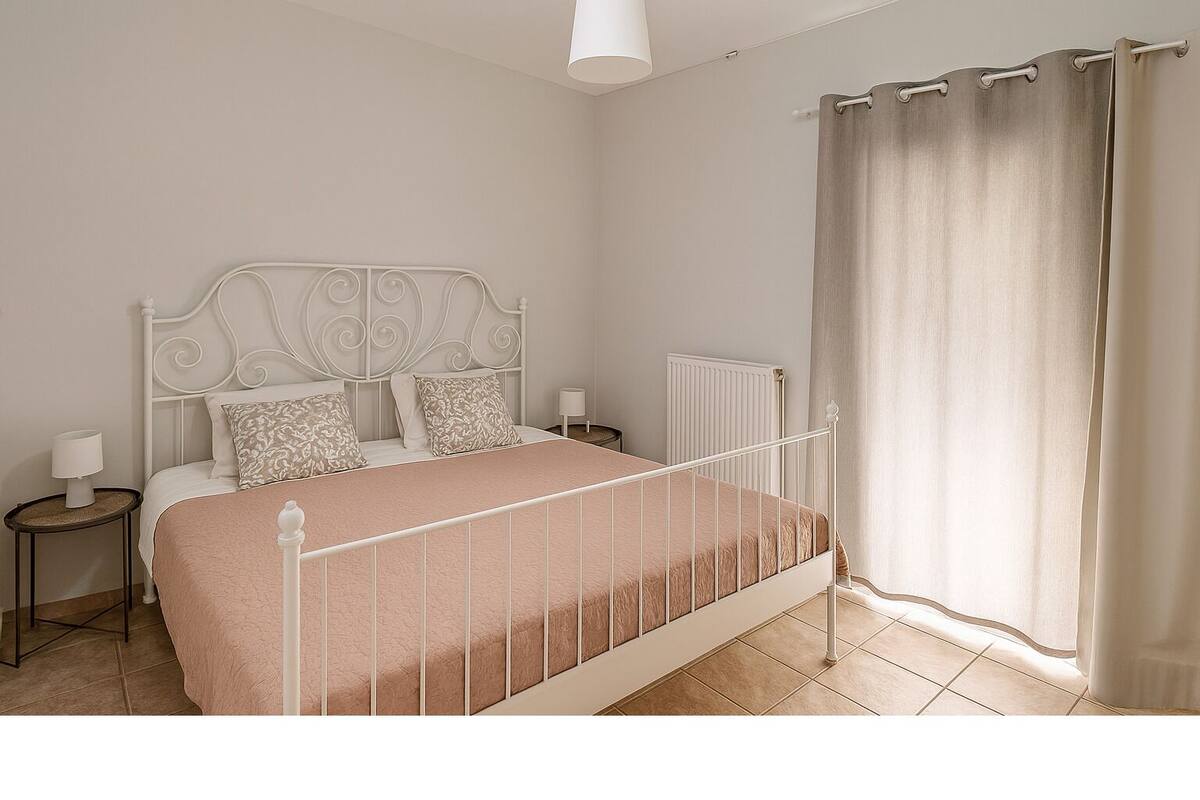 A bedroom with a bed, nightstands, a radiator, and a window with curtains.