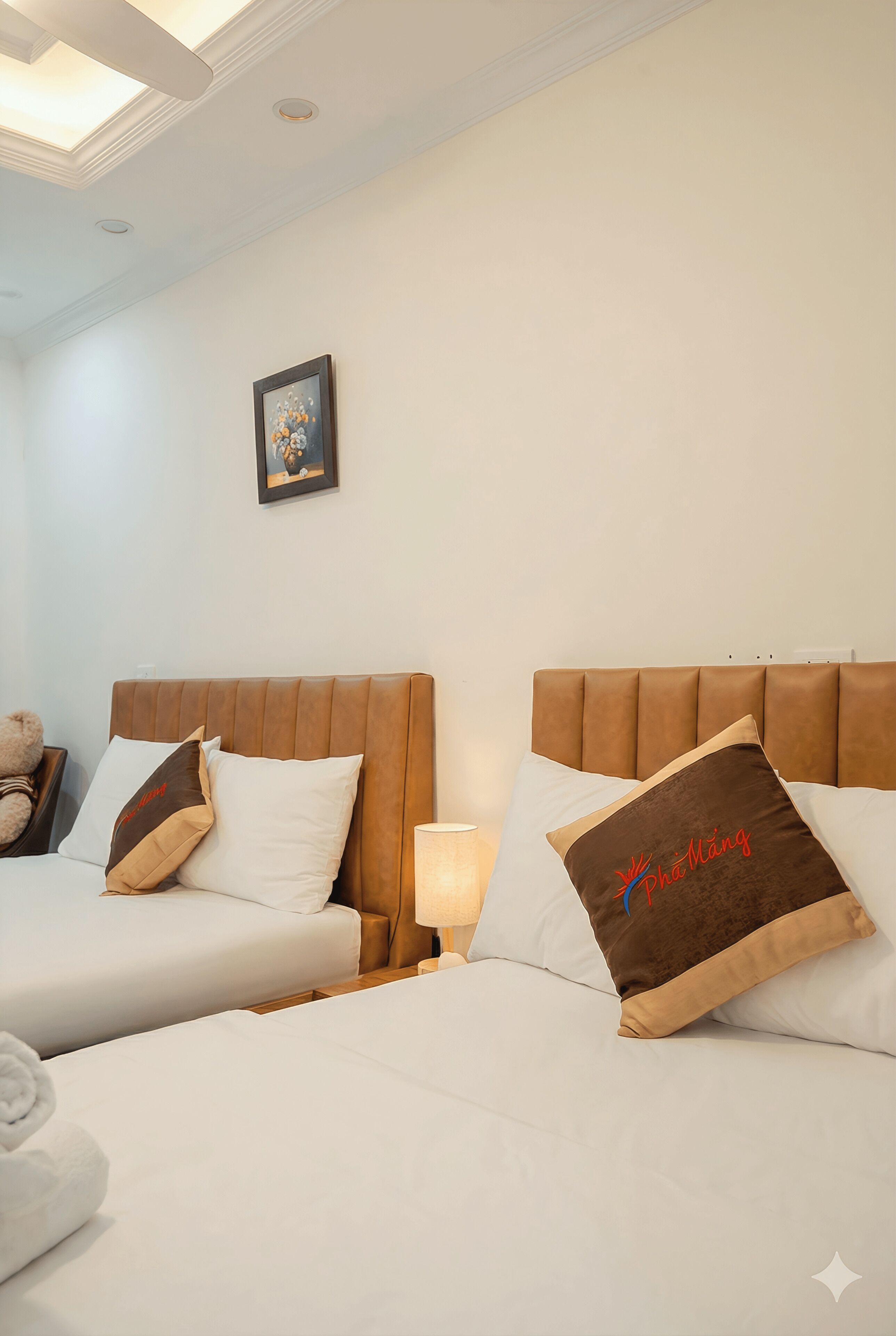 A hotel room with two beds, a bedside table with a lamp, a framed picture on the wall, and a teddy bear on the left bed.