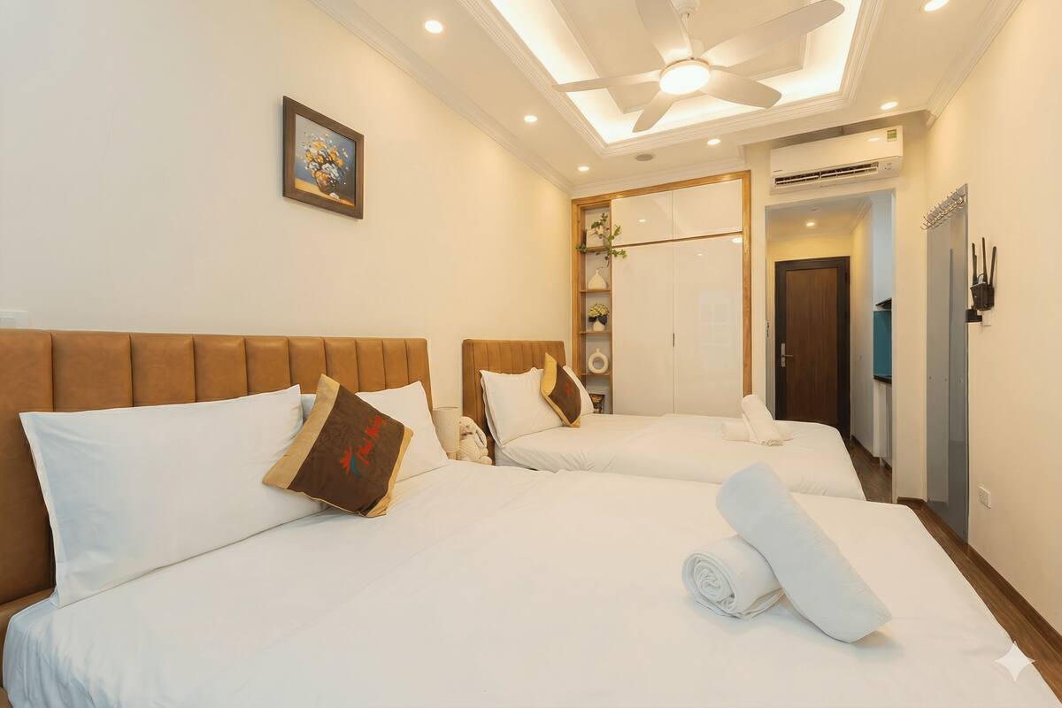 A hotel room with two beds, a ceiling fan, a painting, and an air conditioning unit.