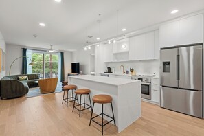 A modern kitchen with a central island, bar stools, stainless steel appliances, and a dining area with a sofa and coffee table. - Chic South Lamar | Pool, Restaurant, Bar, Terrace, Creative Space | The Code (Austin)