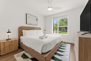 A bedroom with a bed, a nightstand, a desk, a ceiling fan, a window, and a wall-mounted TV. - Chic South Lamar | Pool, Restaurant, Bar, Terrace, Creative Space | The Code (Austin)