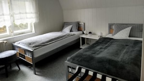 Ein Zimmer mit zwei Einzelbetten, einem kleinen Schreibtisch, einem Stuhl und einem Fenster.