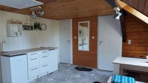 Eine kleine Küche mit weißen Schränken, einer Arbeitsplatte und einem Spiegel. Eine Tür führt in einen anderen Raum, und ein kleiner Tisch bietet einen Sitzkissen.