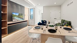 Ein modernes Wohnzimmer mit Essbereich, einem an der Wand montierten Fernseher und einer Couch mit Kissen.