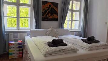 Un dormitorio con una cama grande, dos ventanas con cortinas, un cuadro en la pared y una lámpara en el techo.