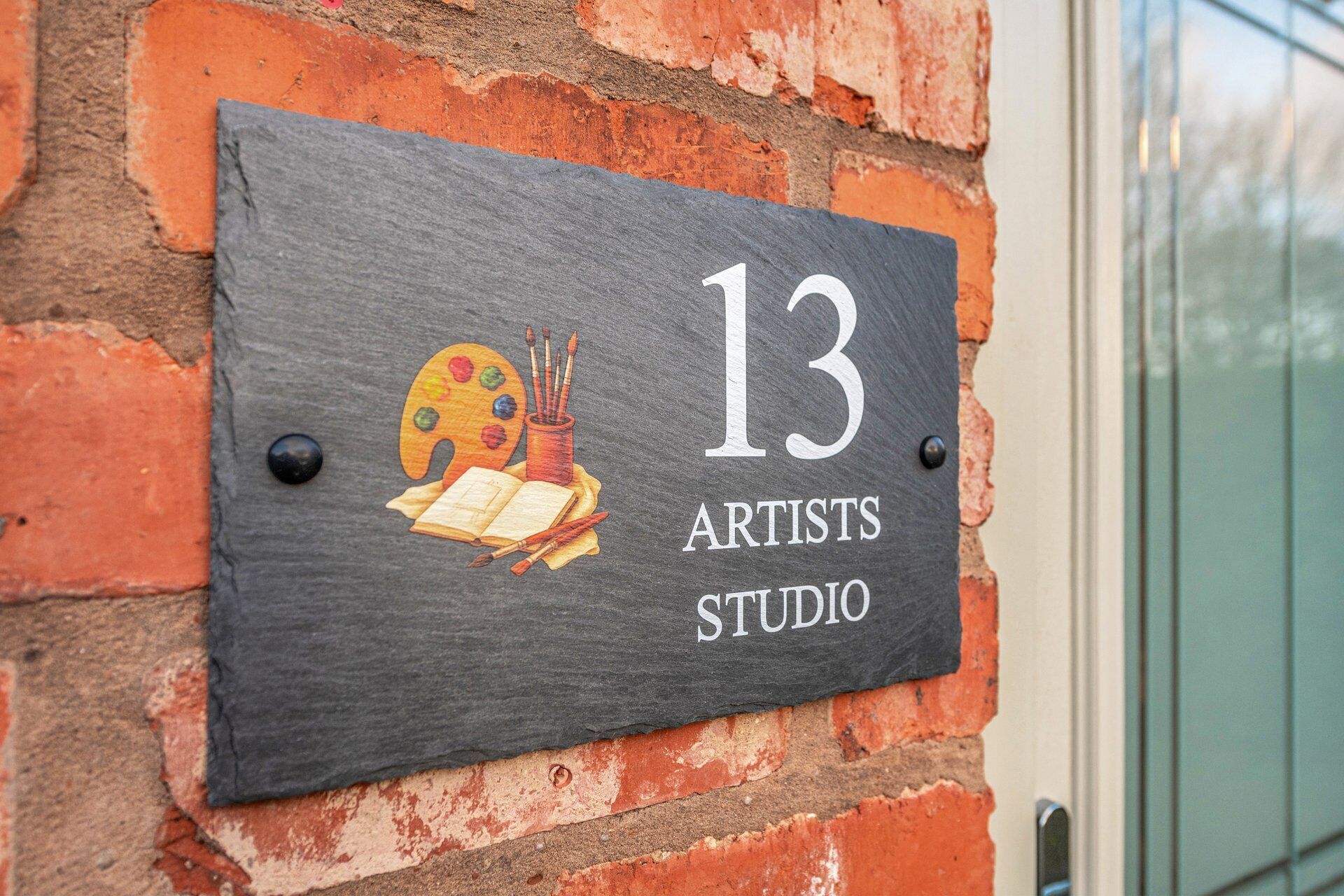 A slate sign with the number 13 and the words 'Artists Studio' on a brick wall.