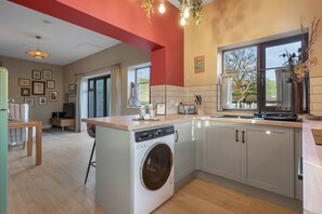 A modern kitchen with a built-in washing machine, a dining area with a table and chairs, and a view of the outdoors through a window.