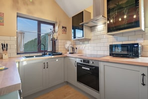 A modern kitchen with a window, a microwave, an oven, and a sink. - Pools Cottage 5 - Racquet Room Close to Warwick (Warwickshire)