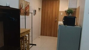 A room with a wooden door, a small table with a chair, a television, and a refrigerator. - Cozy Condo Near US Embassy in Manila (Manila)